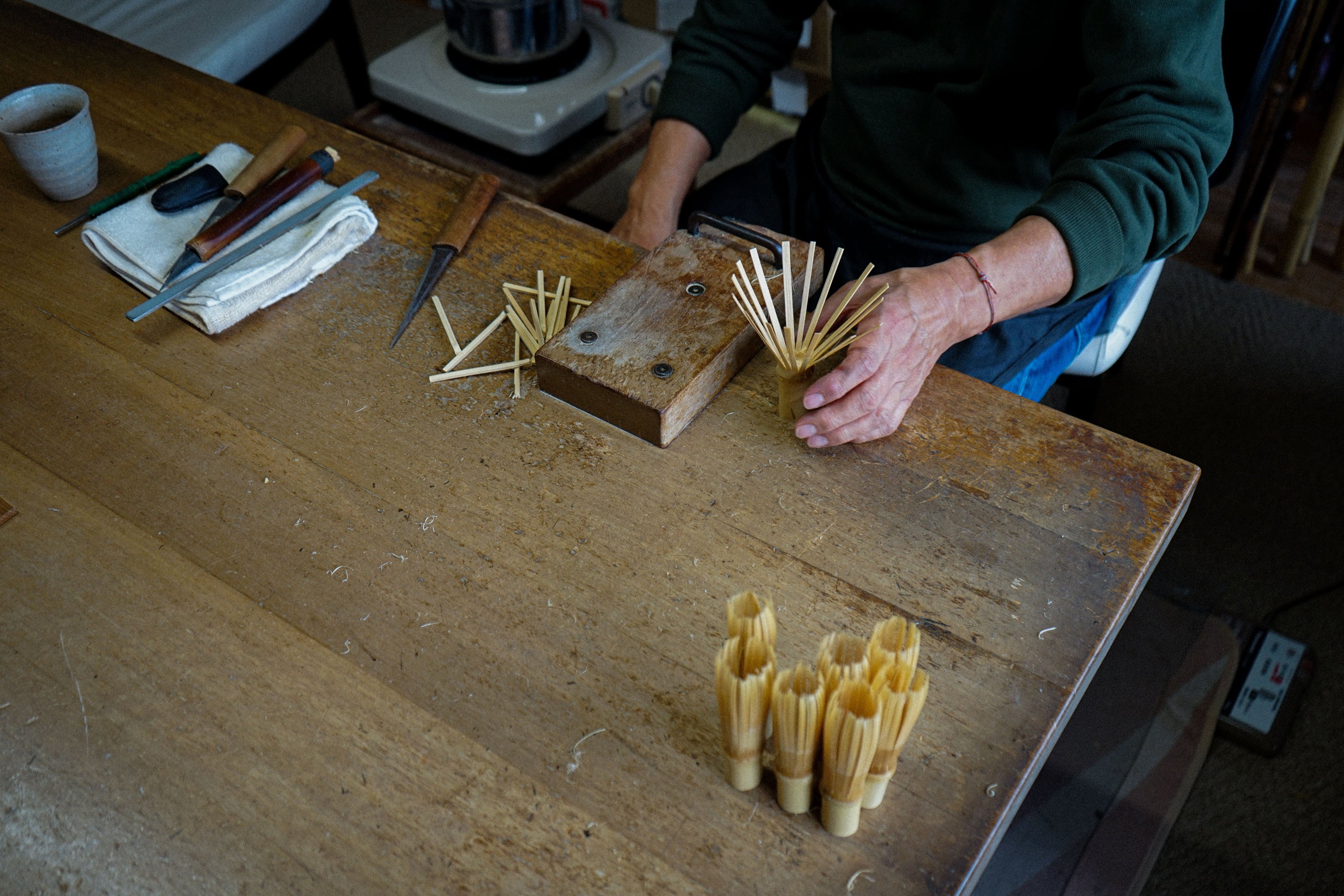 A person's hands arranging dried pasta sticks on a rustic wooden workbench, with several small bundles of pasta sticks standing upright in the foreground.